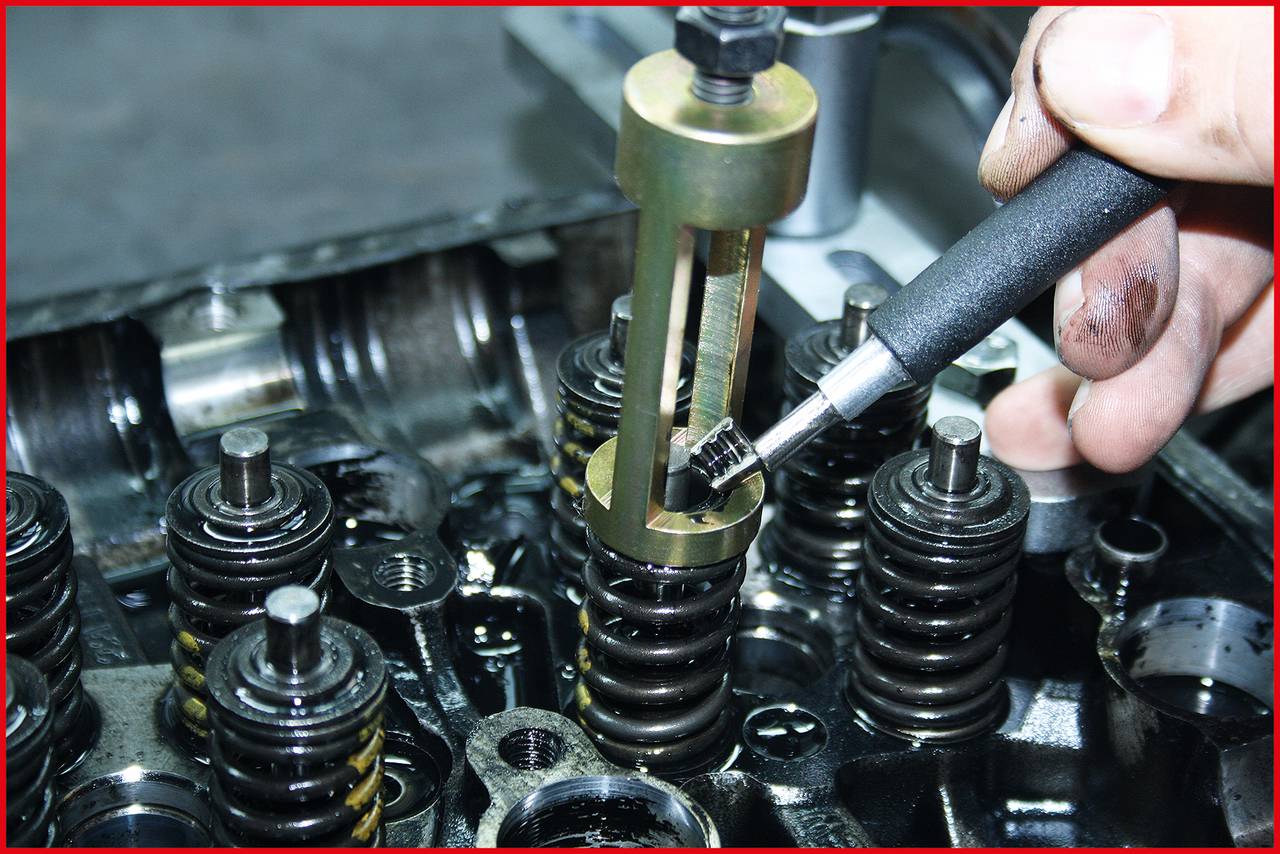 Eine Hand verwendet ein spezielles Werkzeug, um eine Ventilfeder in einem Motor zu bearbeiten. Der Motor ist teilweise zerlegt.