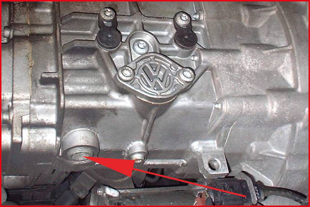 'Nahaufnahme eines Getriebes mit einem Pfeil, der auf eine bestimmte Stelle zeigt. Das VW-Logo ist auf dem Gehäuse sichtbar.'