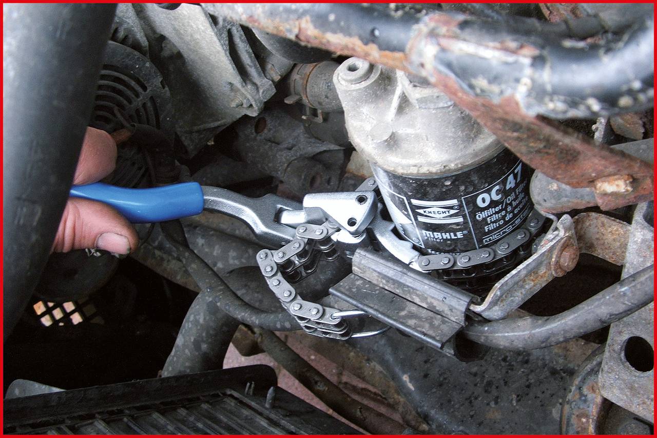 Eine Person verwendet eine Kettenzange, um einen Ölfilter in einem Fahrzeugmotorraum zu entfernen.