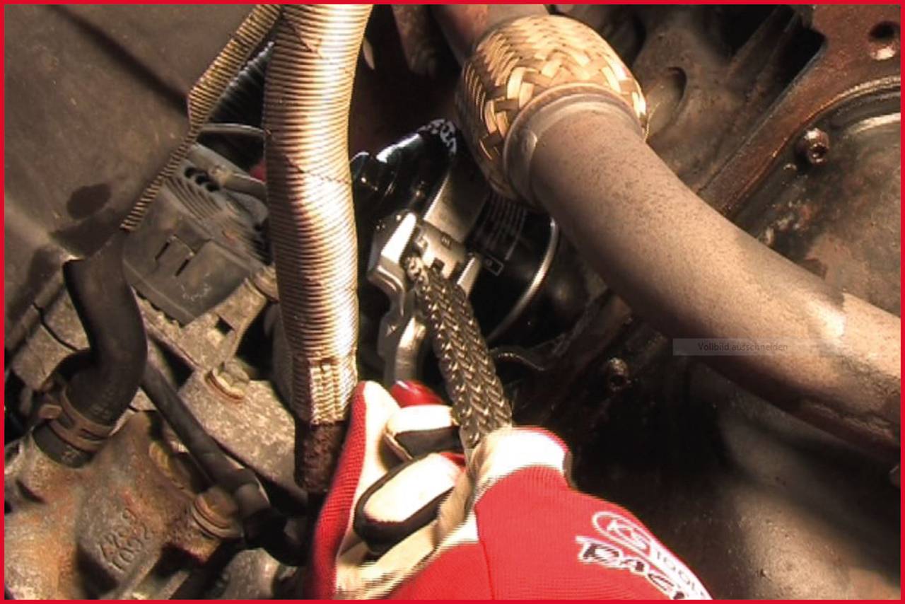 'Arbeiter mit roten Handschuhen befestigt eine Kette an einem Autoteil im Motorraum.'