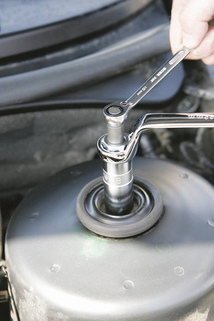 Eine Hand hält einen Schraubenschlüssel, der auf ein Autoteil angesetzt ist, für eine Reparatur oder Wartung im Motorraum.