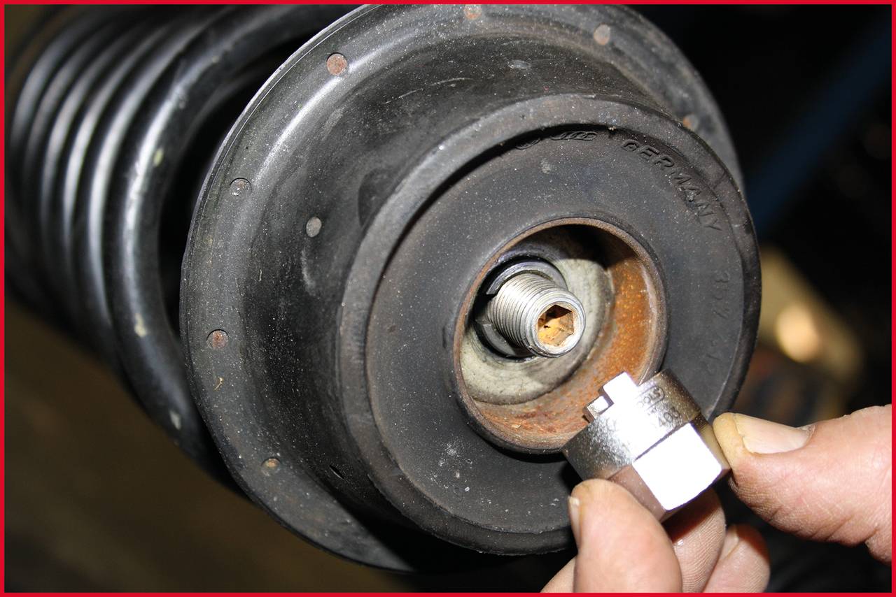 Ein Mechaniker hält eine Metallmutter vor ein Spiralfederelement, das Teil eines Fahrwerks ist. Fokus auf das Gewindeteil.