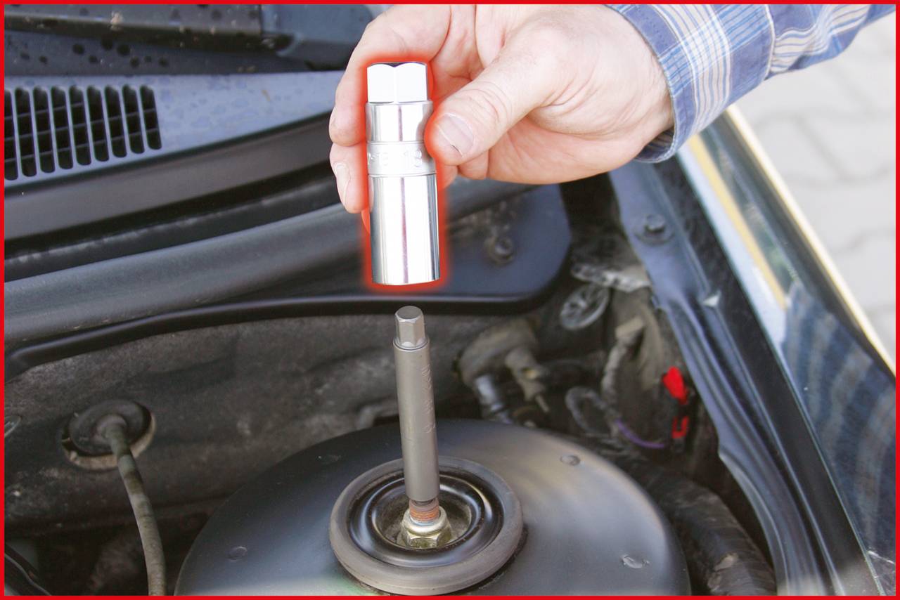 Eine Hand hält eine Zündkerze über dem Motorraum eines Autos, bereit zur Installation oder zum Austausch.