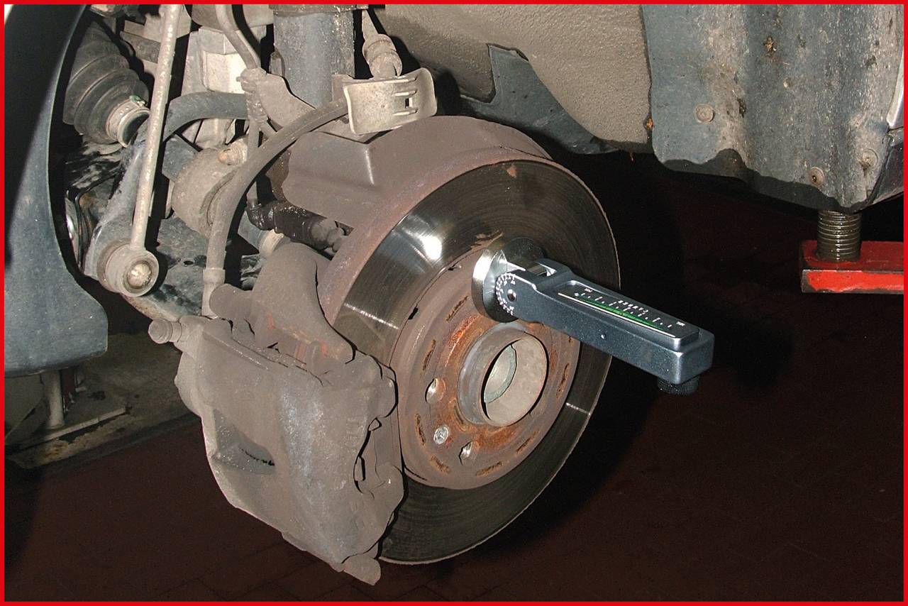 Nahaufnahme eines Autobremsensystems: Eine Bremsscheibe ist mit einem Drehmomentschlüssel am Bremssattel befestigt.