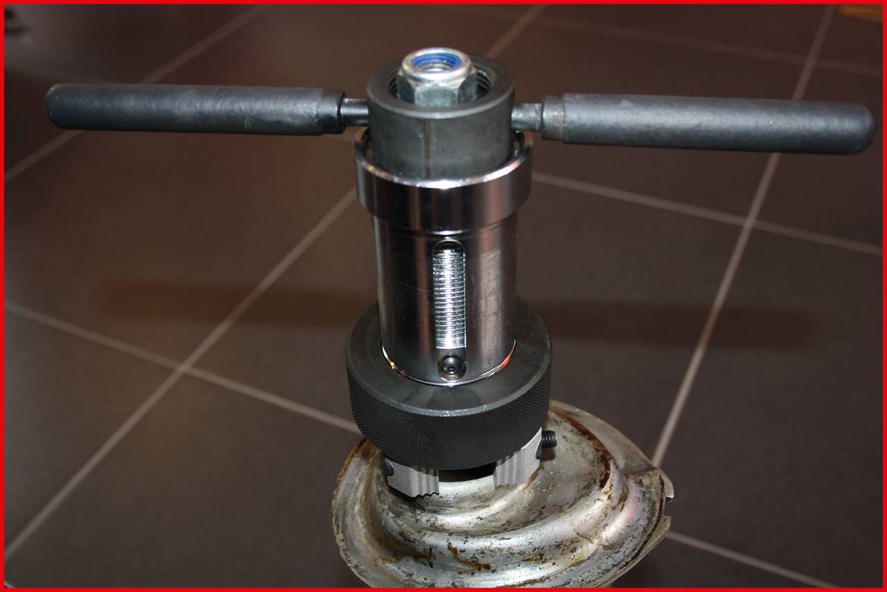 Ein Metallgerät mit zwei Griffen oben, montiert auf einer runden Basis, steht auf einem gefliesten Boden.