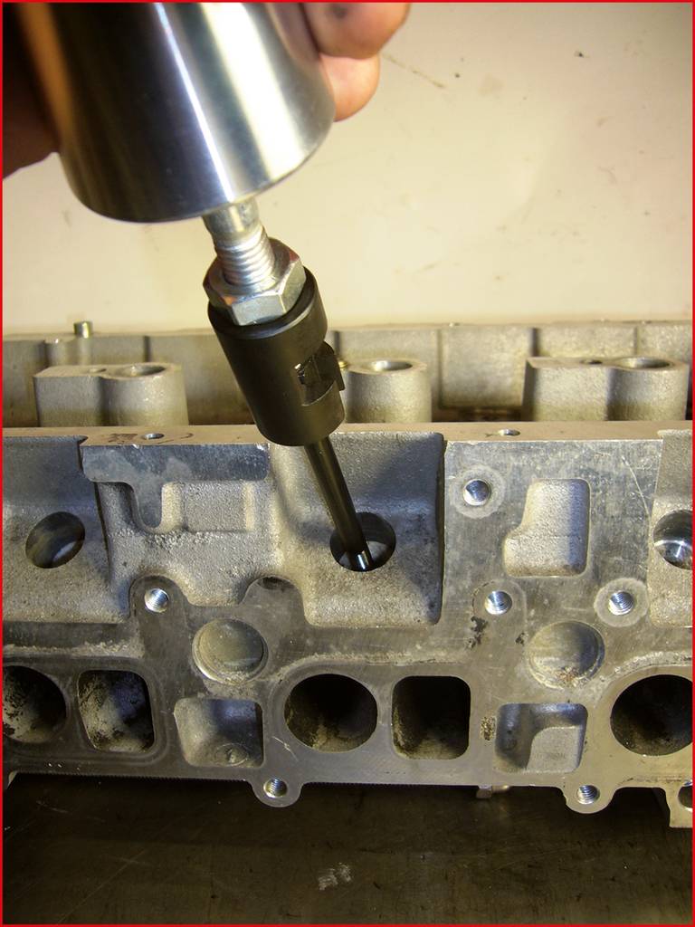 'Hand hält Werkzeug, das eine Metallkomponente an einem Motorblock bearbeitet.'