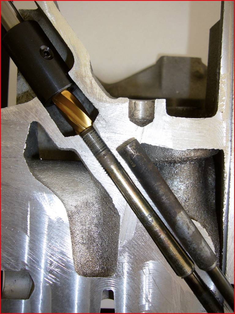 Ein Metallblock zeigt eine vertikale Bohrung mit einem mehrfarbigen Bohrwerkzeug und einer Stange, die beim Bearbeiten verwendet werden.