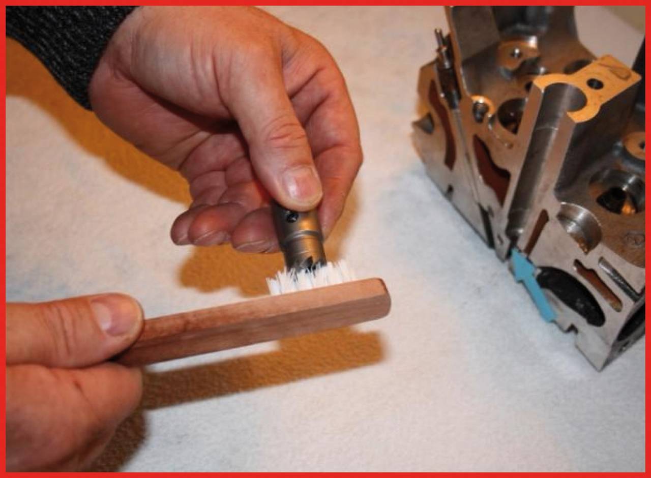 Eine Person reinigt mechanische Teile mit einer kleinen Bürste auf einem Tisch. Rechts im Bild liegt ein Metallbauteil.