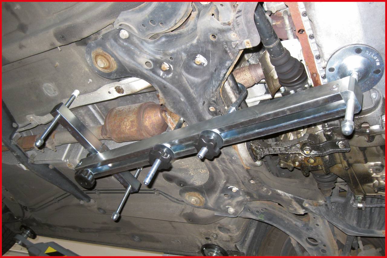 Ein Gestell hält ein Fahrzeugteil im Motorraum. Sichtbar sind Schrauben und Achse. Es zeigt einen Teil einer Fahrzeugreparatur oder -wartung.