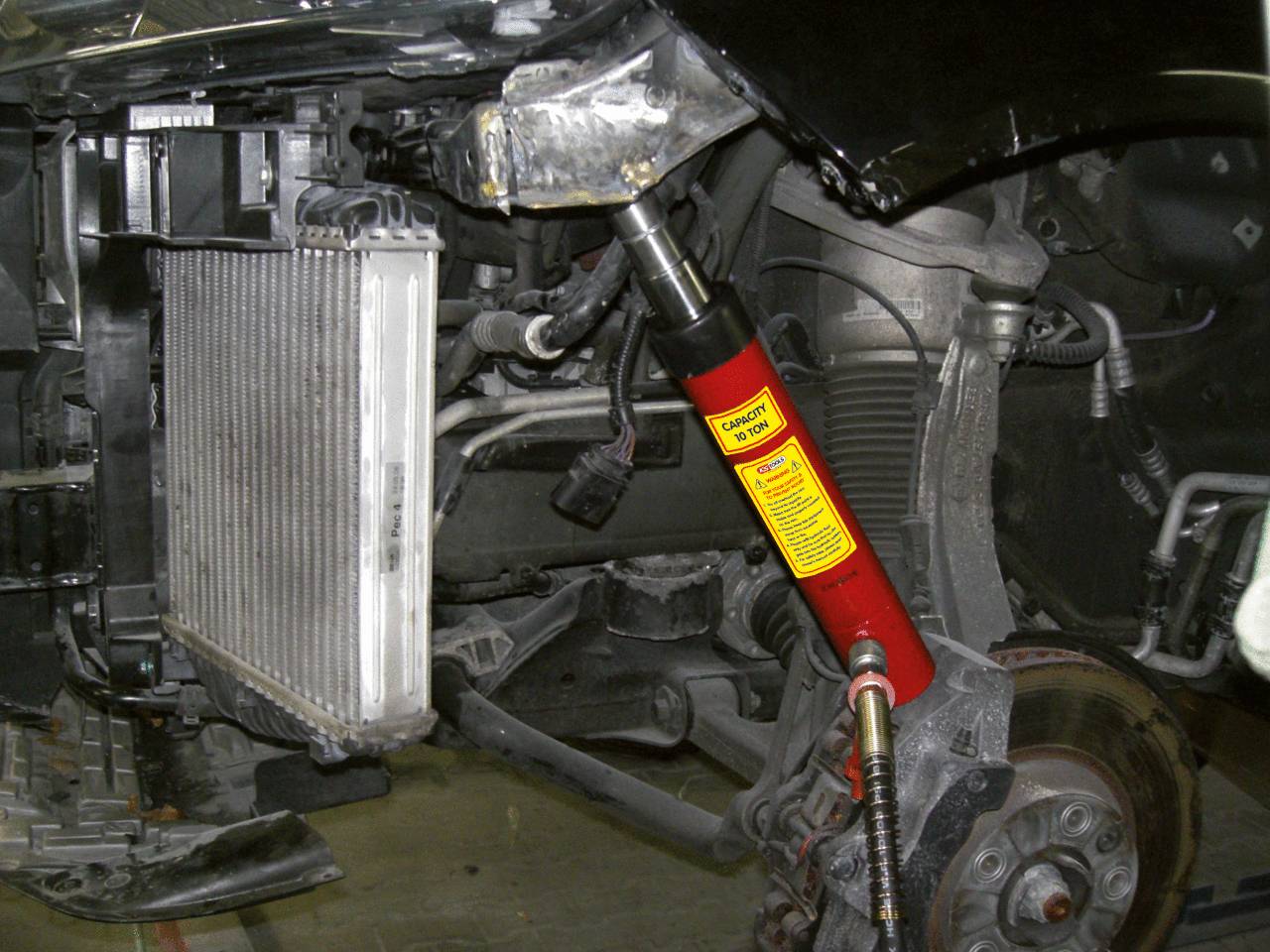 Ein Auto mit geöffneter Motorhaube, sichtbarem Kühler und Stoßdämpfer. Mechanische Komponenten werden zur Reparatur bearbeitet.