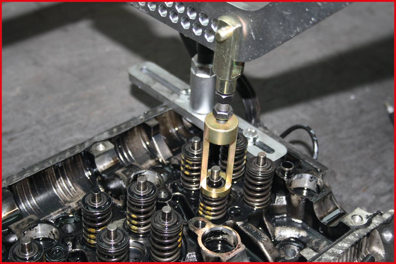 Ein Metallwerkzeug hebt ventilähnliche Komponenten in einem Motorblock an. Der Hintergrund ist unscharf und grau.