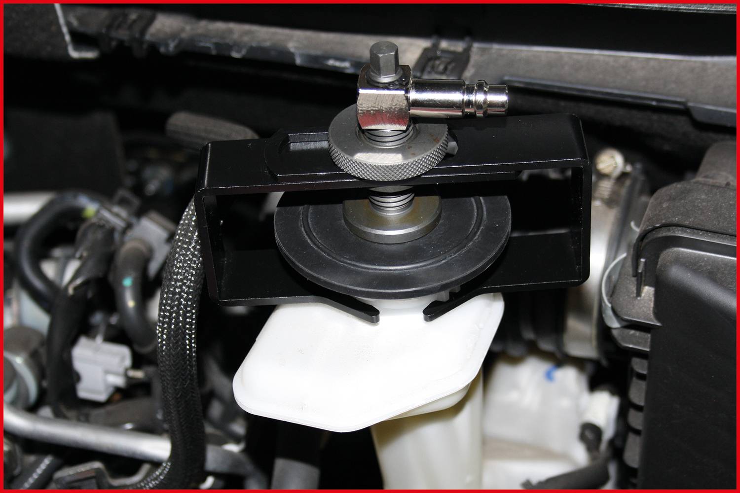 Ein Werkzeug zieht mit einem Abzieher-Flansch einen Kugellager von einem schwarzen Metallstück ab, umgeben von Autoteilen.