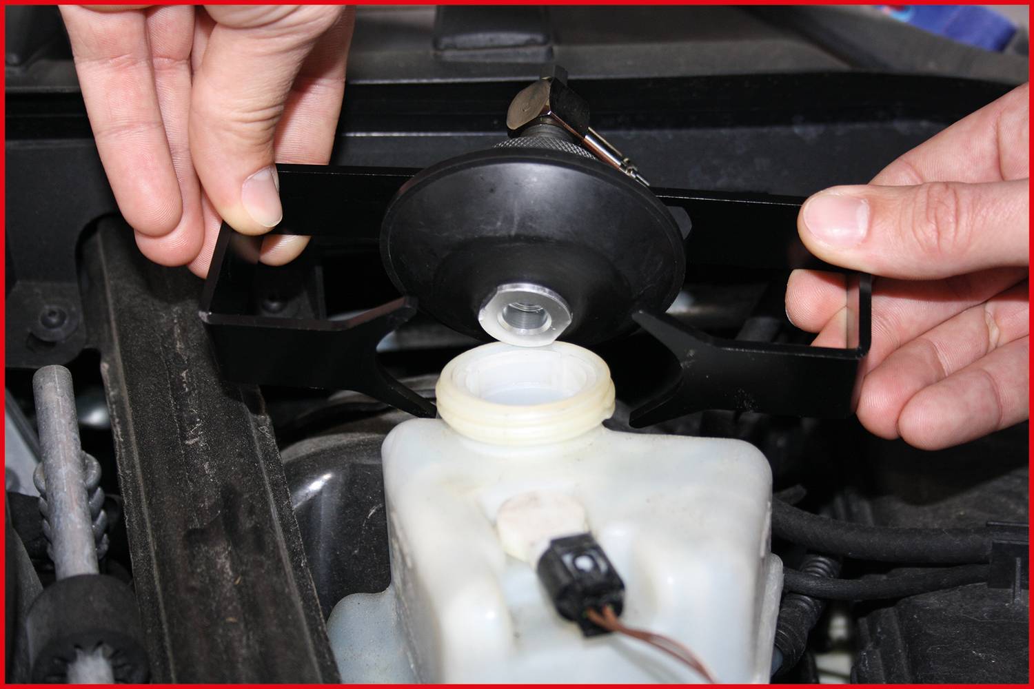 Zwei Hände entfernen den Deckel eines Bremsflüssigkeitsbehälters im Motorraum eines Autos. Der Behälter ist teilweise gefüllt.