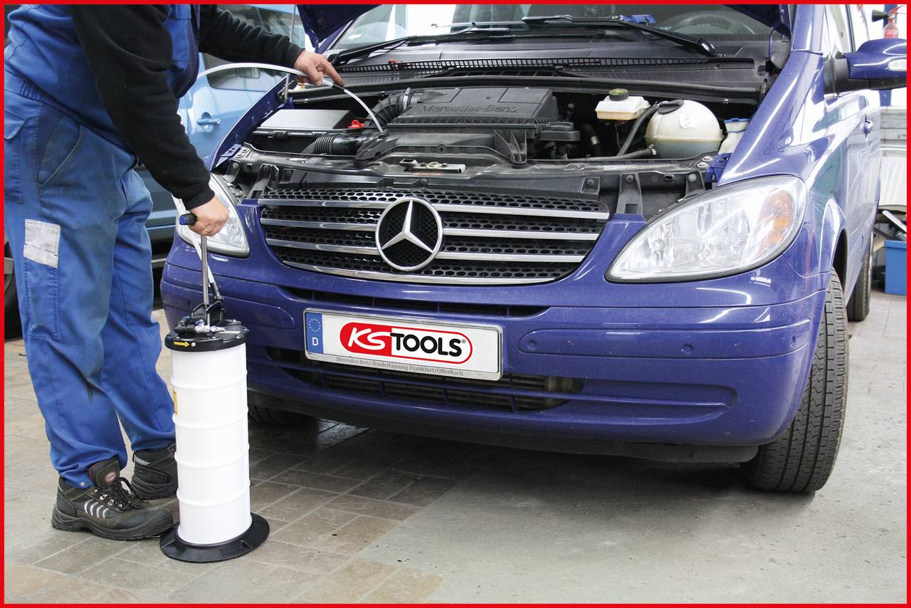 Mechaniker führt einen Ölwechsel an einem blauen Auto durch, indem er eine Absaugpumpe verwendet; Motorhaube ist geöffnet.