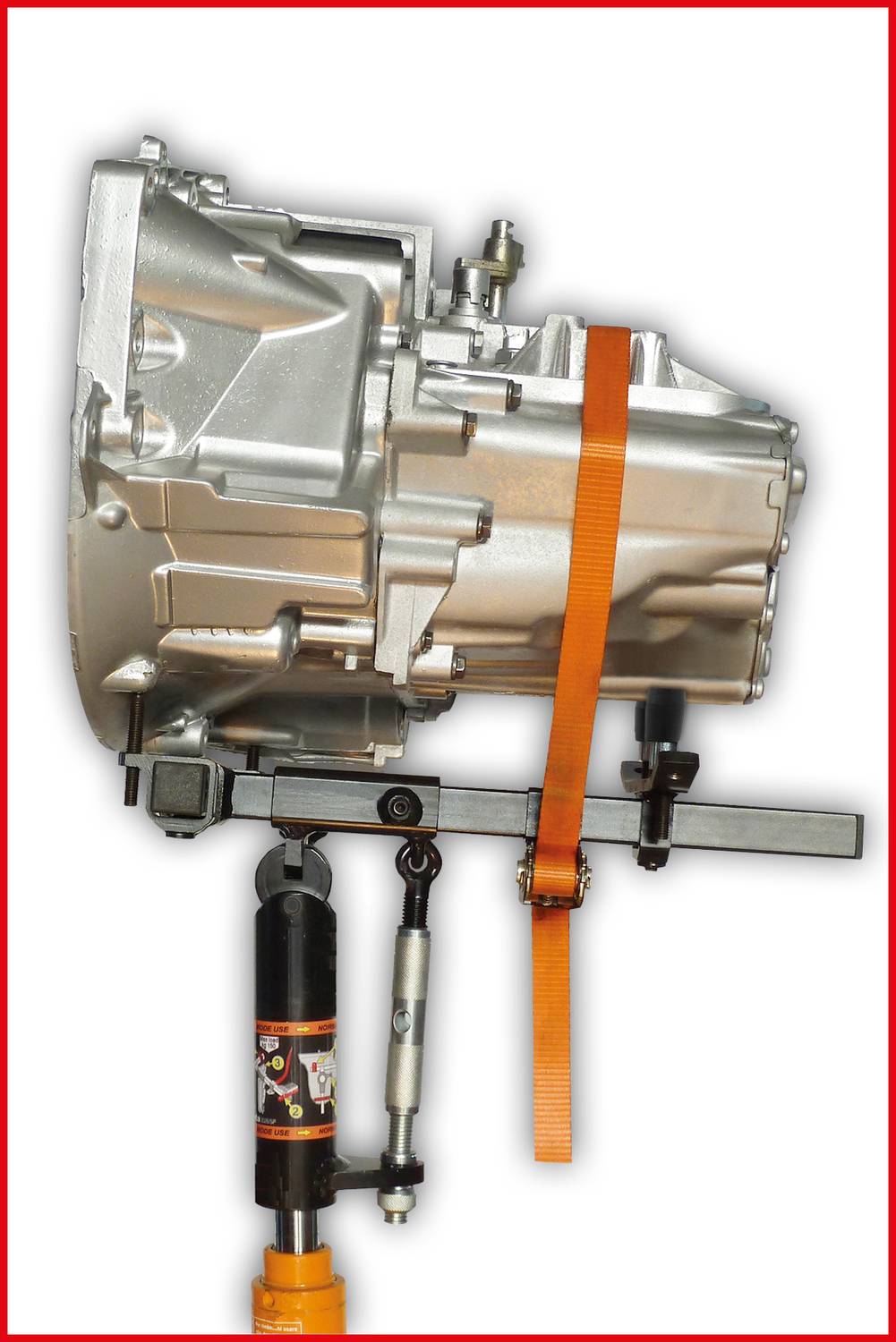 'Getriebe in silberner Farbe, gesichert mit einem orangefarbenen Gurt und montiert auf einer hydraulischen Hebevorrichtung.'