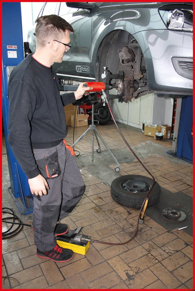 Mechaniker arbeitet an einem angehobenen Auto in einer Werkstatt. Er bedient ein Werkzeug zur Bearbeitung eines Rades.