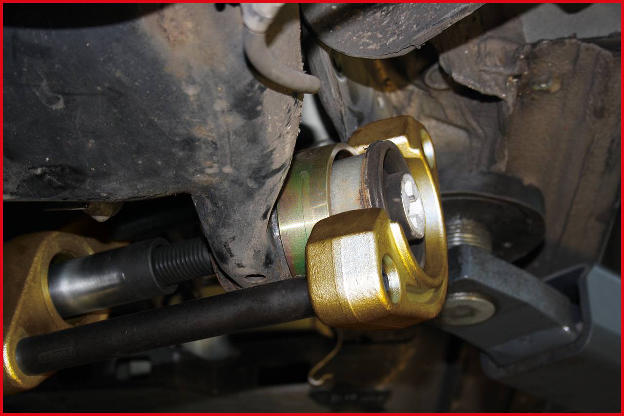 Nahaufnahme eines Autoteils unter dem Fahrzeug, zeigt eine Schraubvorrichtung, die an Metallelementen befestigt ist, möglicherweise zur Wartung oder Reparatur.