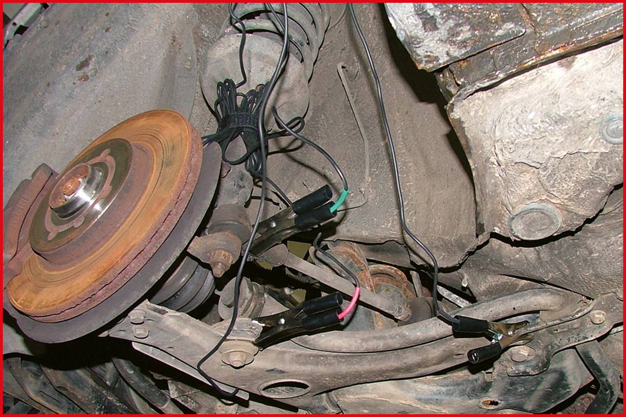 Auto-Bremsscheibe mit angeschlossenen Messgeräten und Kabeln. Die Szene zeigt eine Reparatur oder Diagnose am Fahrwerk eines Fahrzeugs.