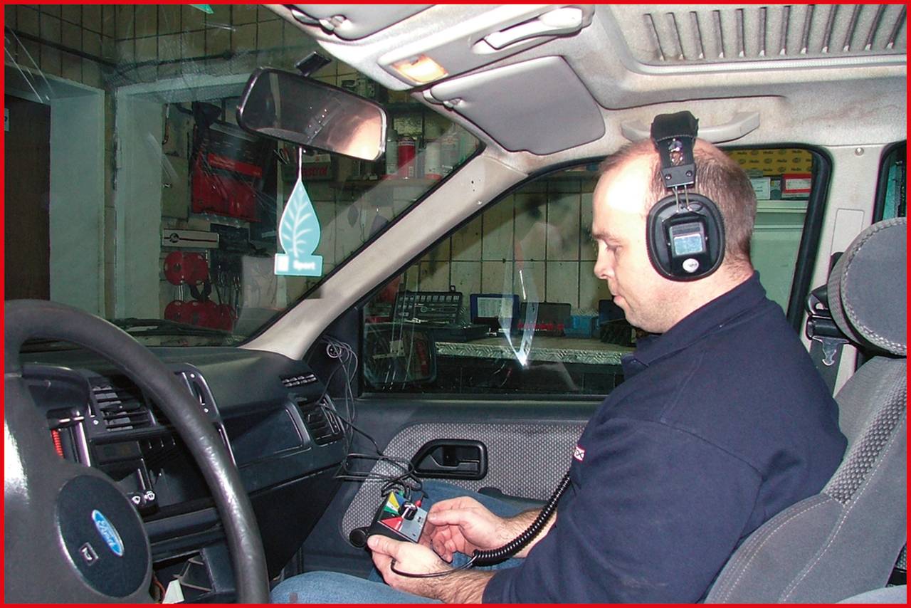 Mann im Auto mit einem Diagnosegerät, trägt Kopfhörer. Er prüft die Fahrzeugdiagnose, um technische Probleme zu identifizieren.