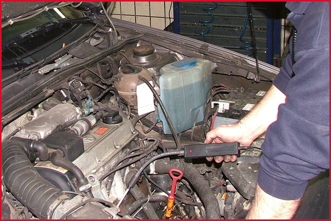 Ein Mechaniker überprüft den Motor eines Autos mit einem Diagnosegerät. Im Vordergrund sind verschiedene Motorkomponenten zu sehen.