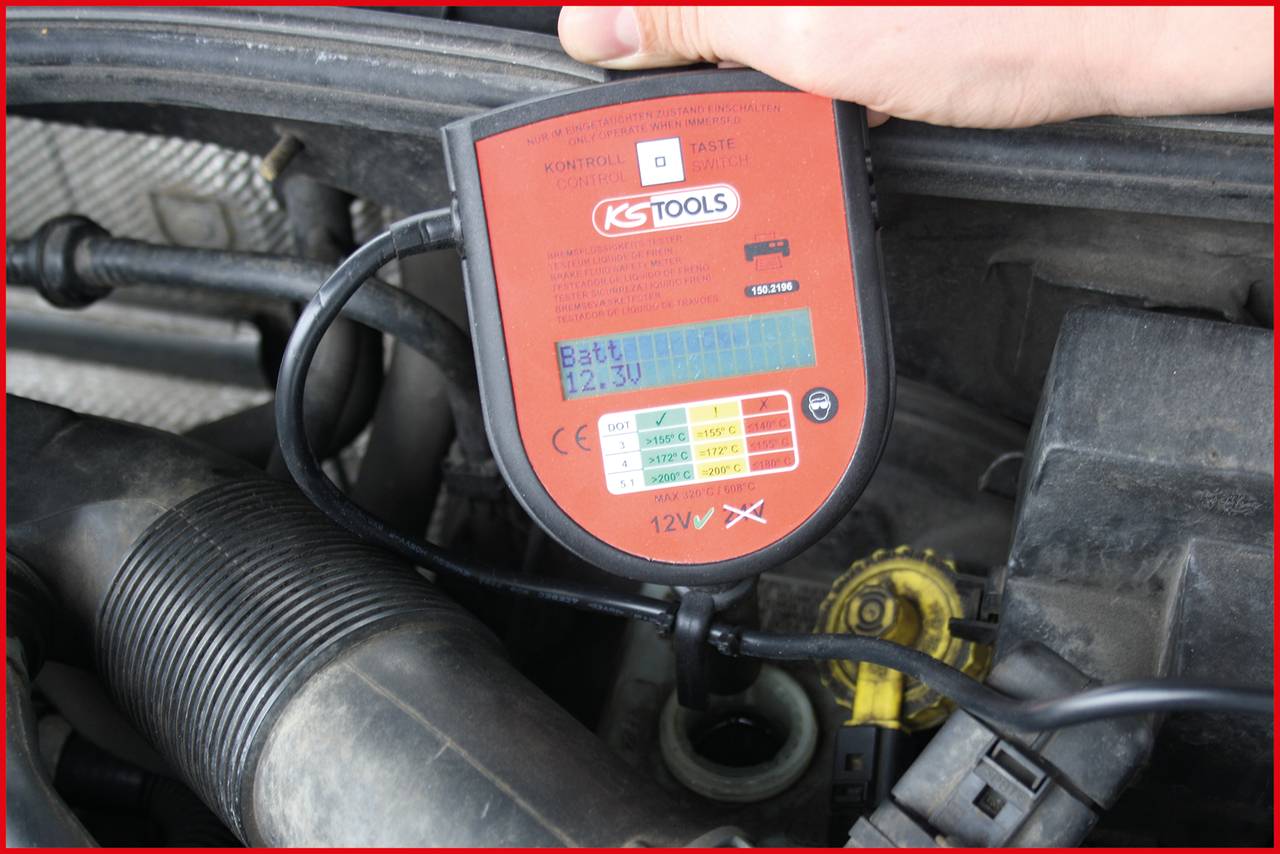 Ein Diagnosegerät zeigt die Batterieladung eines Autos an, die 12,3V beträgt. Es wird über ein Kabel mit dem Fahrzeug verbunden.