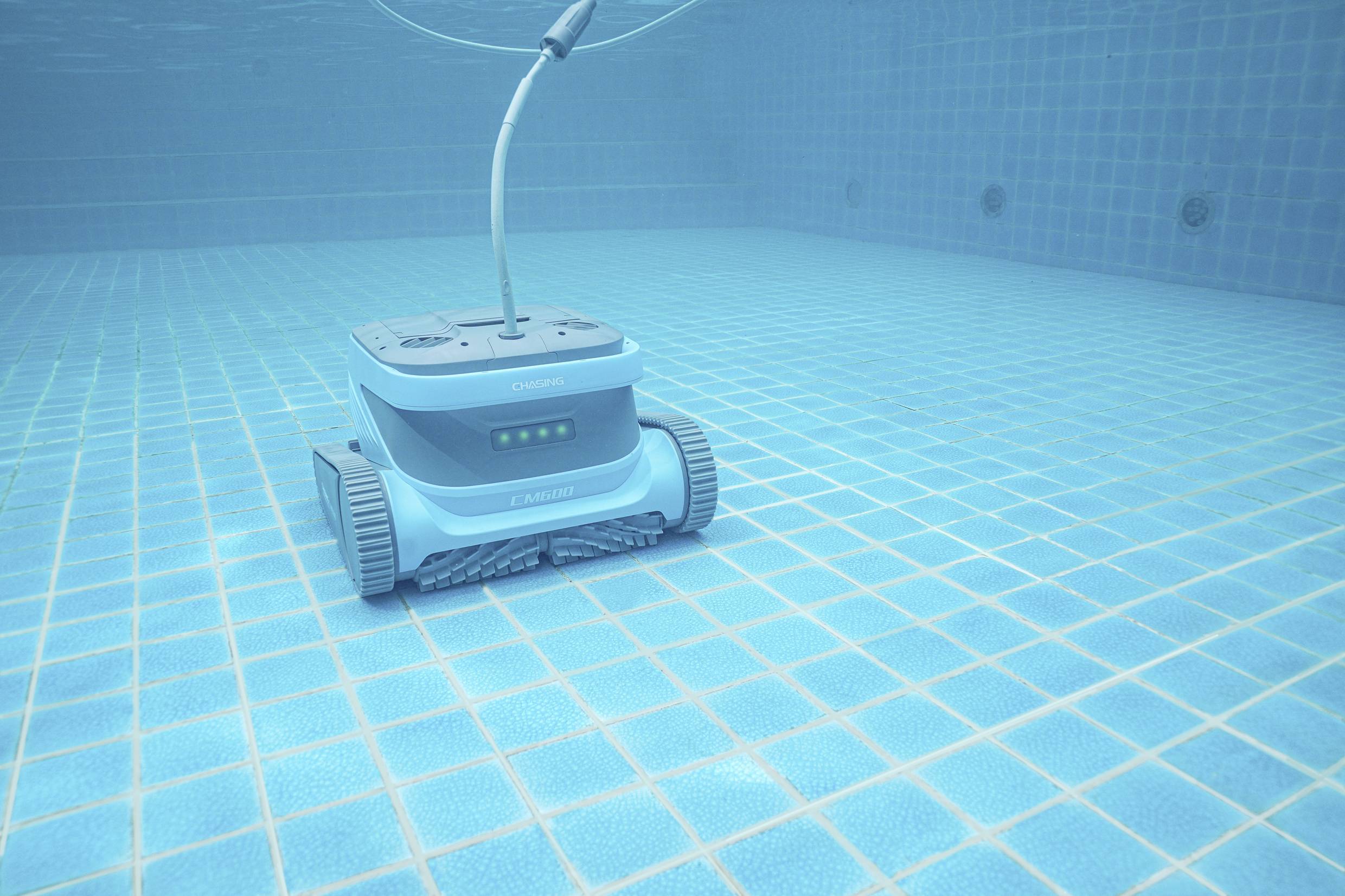 Ein blauer Poolroboter fährt am Boden eines gefliesten Schwimmbeckens entlang, um dieses zu reinigen.