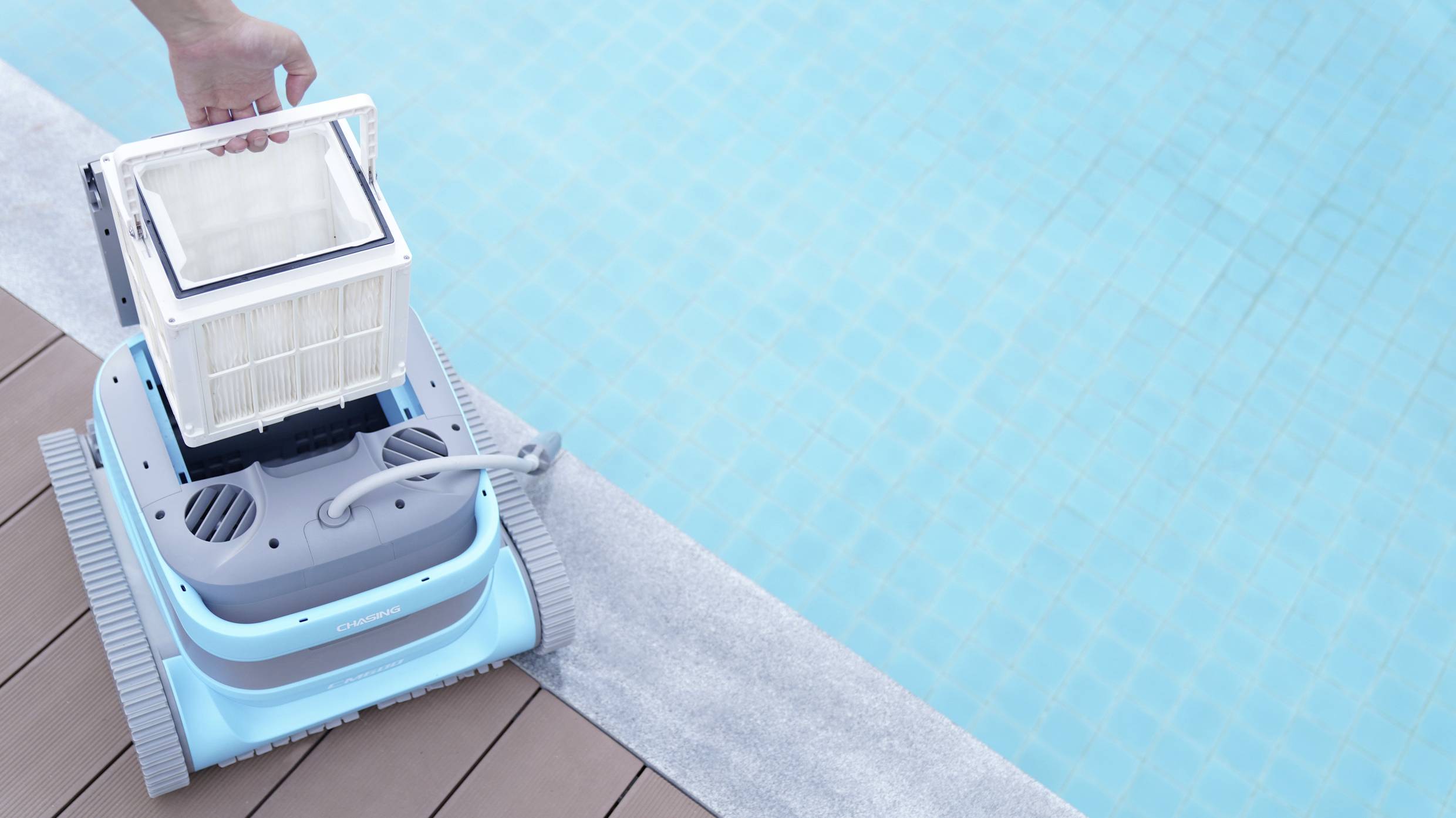 Ein Poolroboter mit herausnehmbarem Filter wird am Beckenrand eines blauen Schwimmbeckens gehalten, bereit zur Reinigung.
