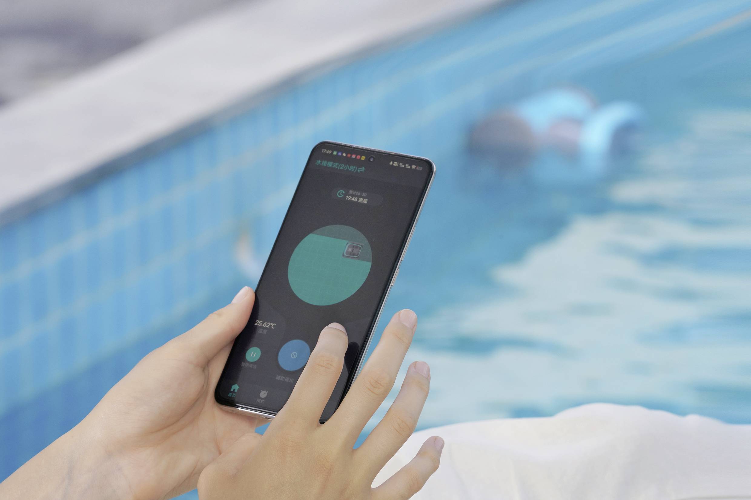 Eine Person hält ein Smartphone neben einem Pool und zeigt eine App mit einem Kreisdiagramm auf dem Bildschirm.