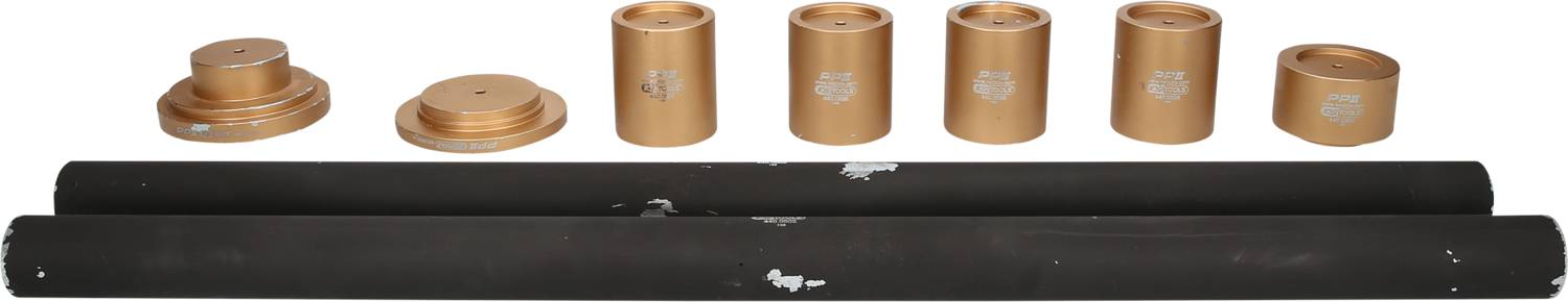 Acht goldfarbene zylindrische Metallstücke und zwei lange schwarze Stäbe liegen nebeneinander auf einer weißen Oberfläche.