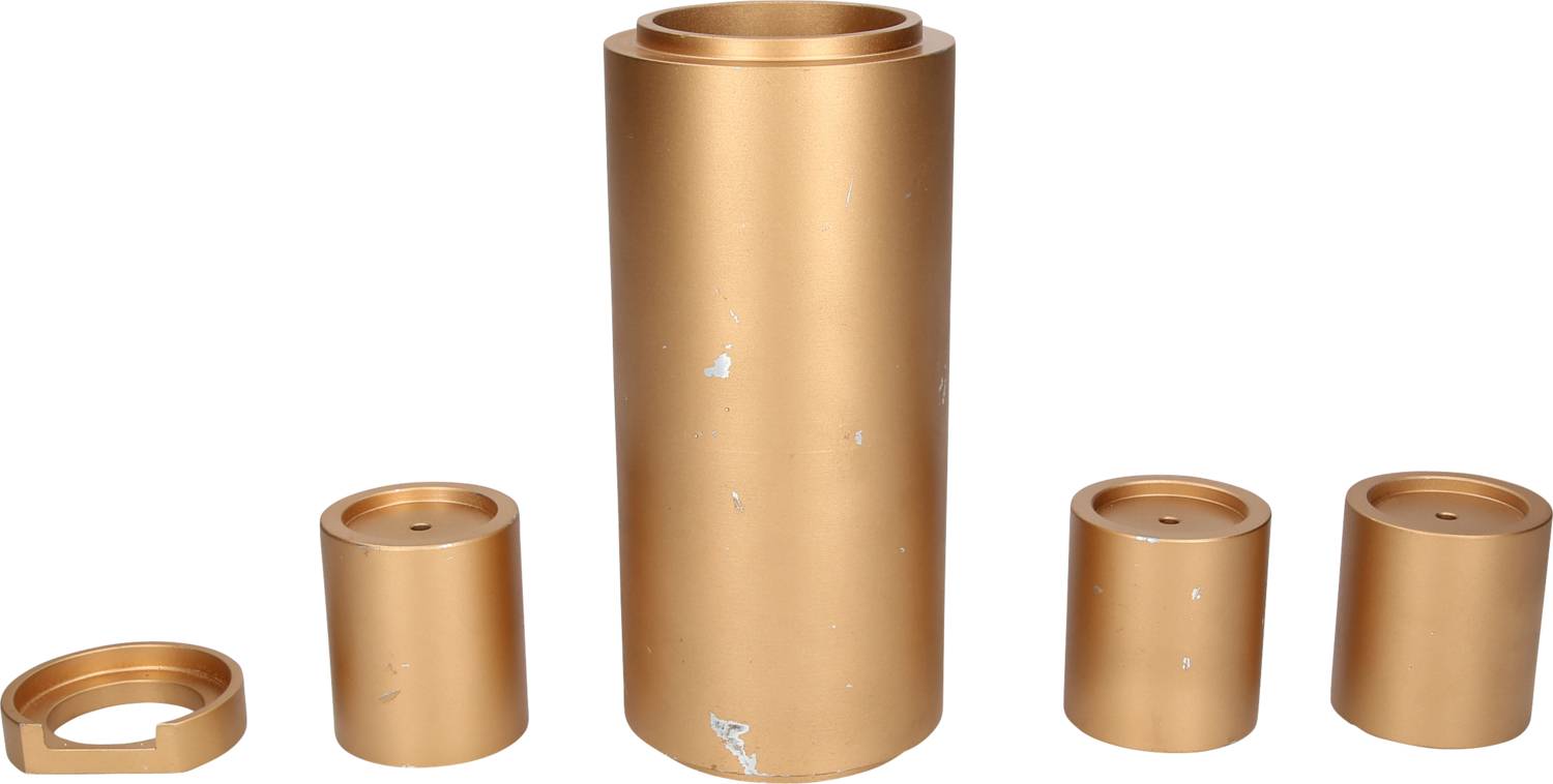 Ein Satz von fünf zylindrischen, goldfarbenen Metallteilen, darunter ein großer zentraler Zylinder und vier kleinere unterschiedlichen Durchmessers.