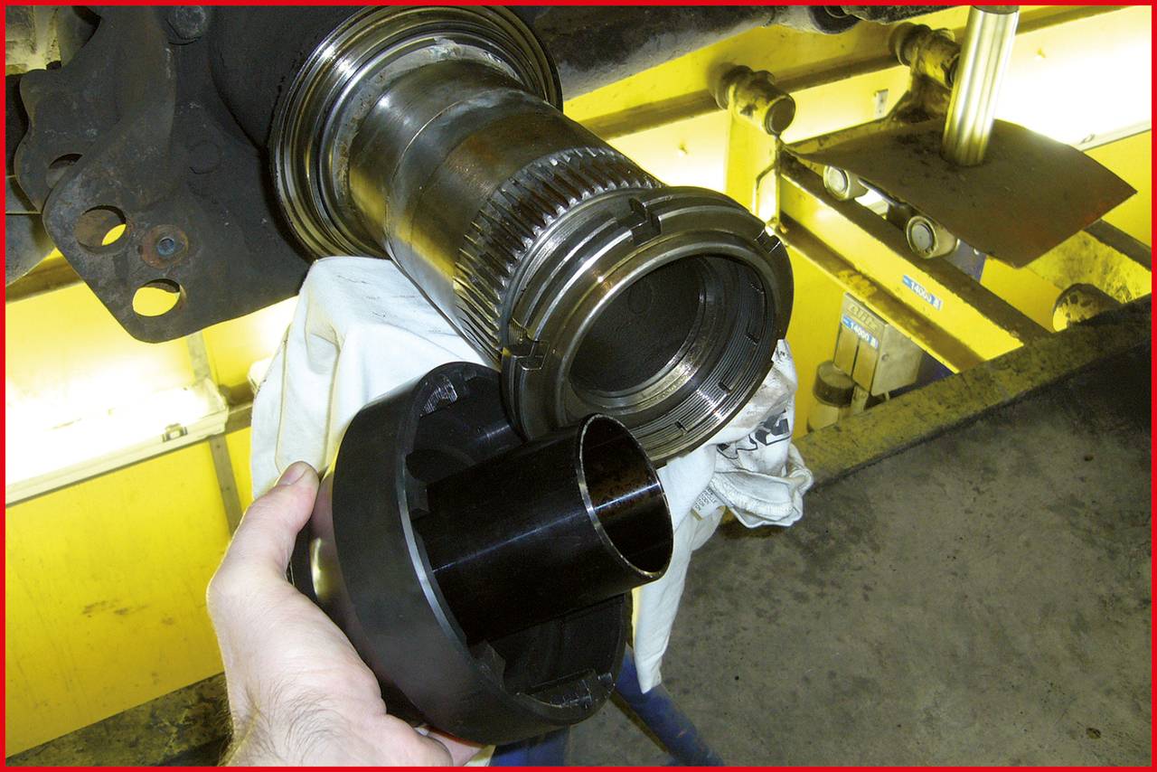 Eine Person hält ein schwarzes Rohrstück, das an einen Metallzylinder angebracht werden soll. Die Szene zeigt eine technische Werkstatt.