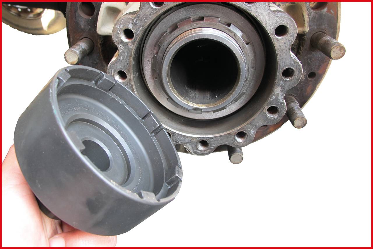 Nahaufnahme eines Autoteils. Eine Hand hält eine schwarze Kappe nahe an einen Metallzylinder mit Schraubenlöchern, möglicherweise ein Teil des Fahrwerks.
