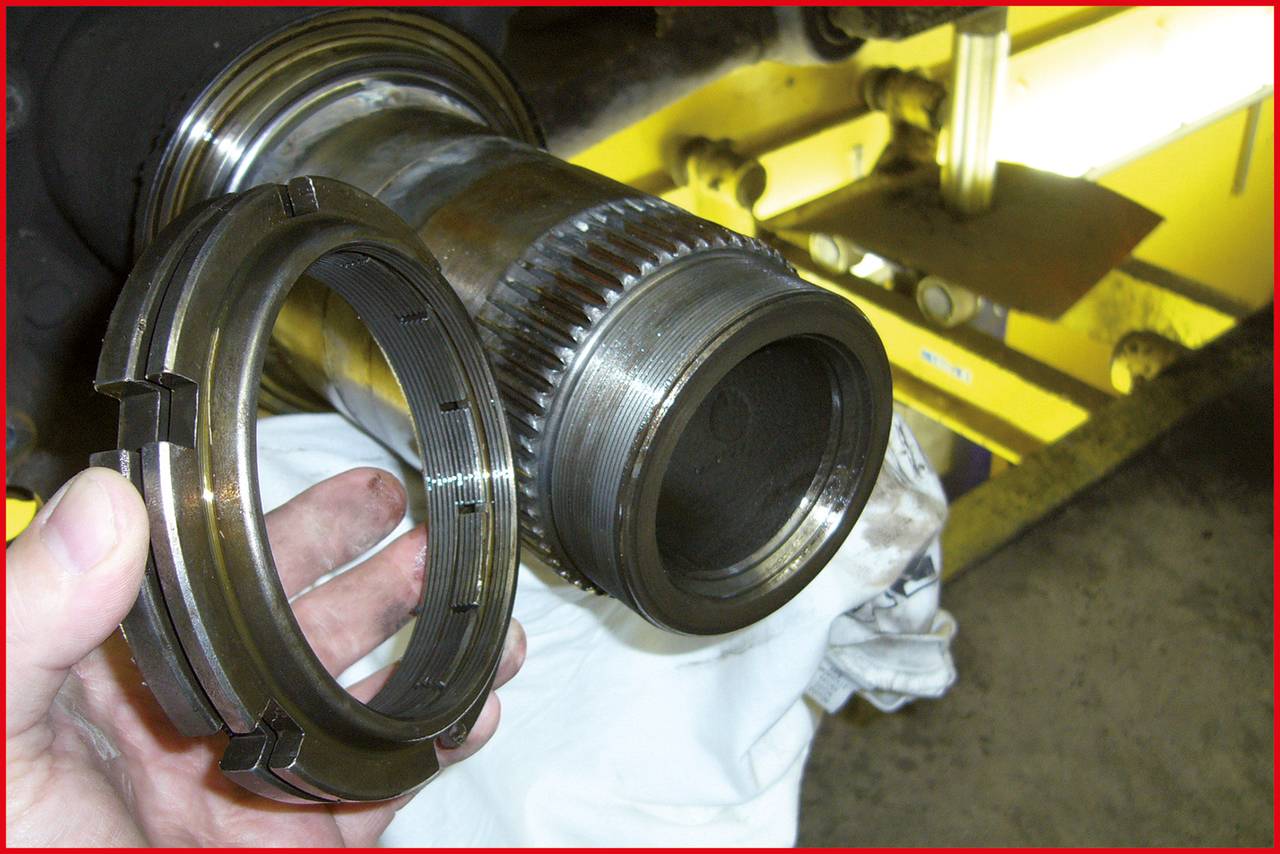 Eine Person hält eine Metallmutter neben einem großen, geriffelten Metallzylinderteil, möglicherweise Teil einer Maschine.