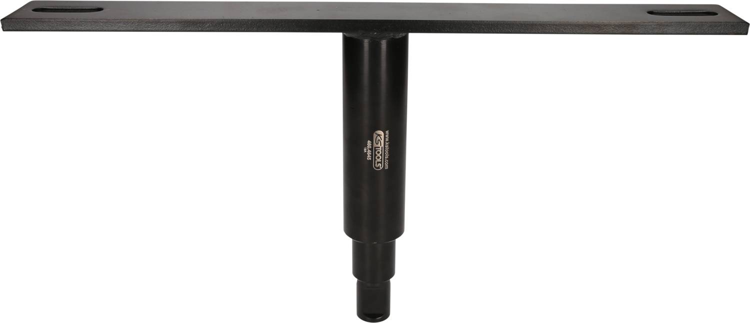 Ein schwarzes, T-förmiges Metallstück mit einer Beschriftung in der Mitte. Es hat zwei Schlitze an den Enden der horizontalen Leiste.