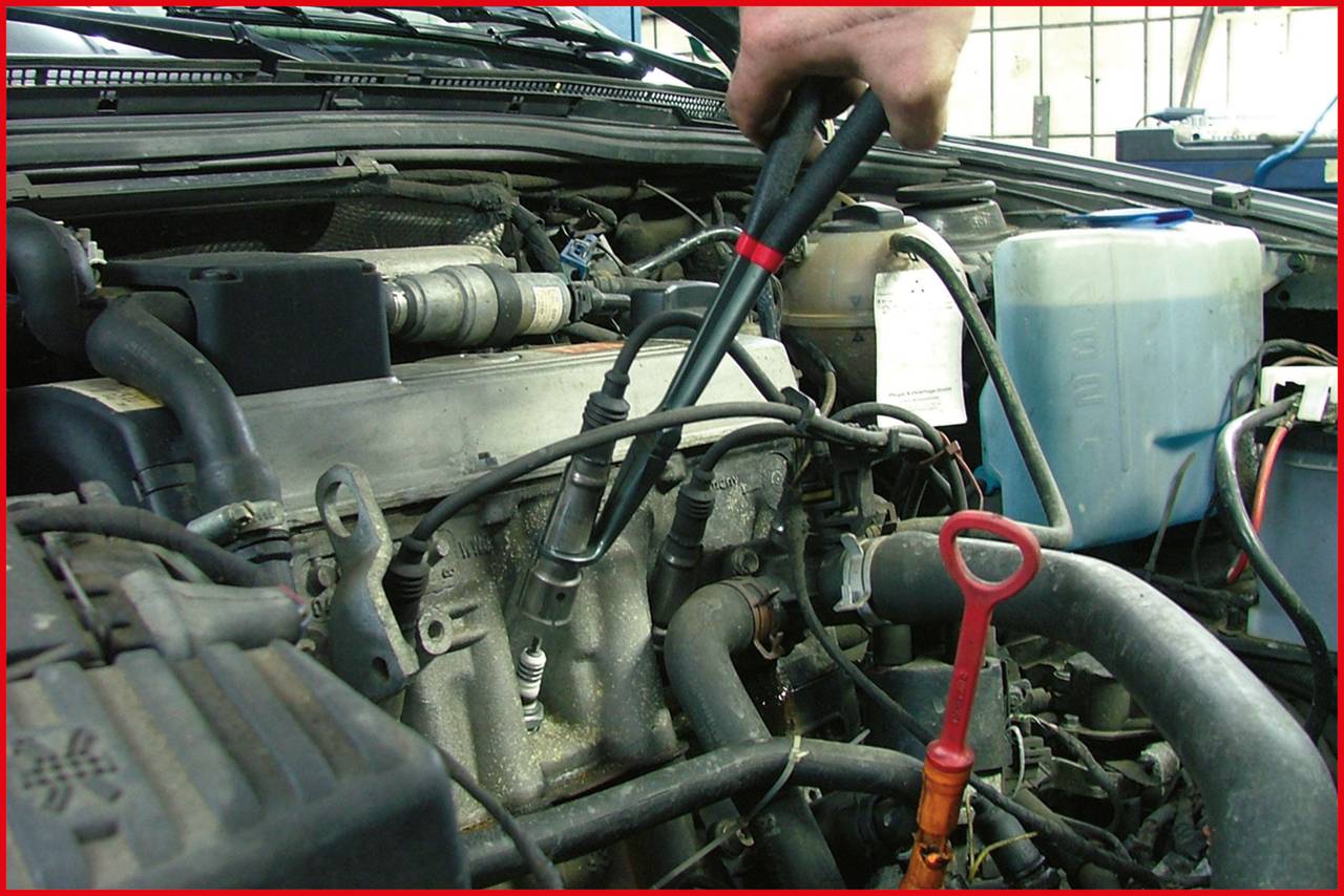 Ein Mechaniker verwendet ein Werkzeug, um eine Zündkerze in einem geöffneten Motorraum eines Autos zu bearbeiten.