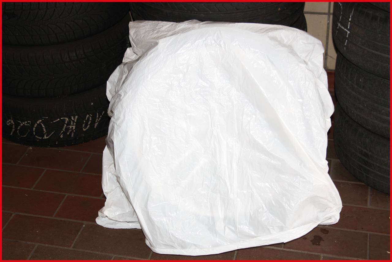 Ein eingepackter Autoreifen in einer weißen Plastikfolie steht auf einem Fliesenboden. Im Hintergrund sind weitere Reifen zu sehen.