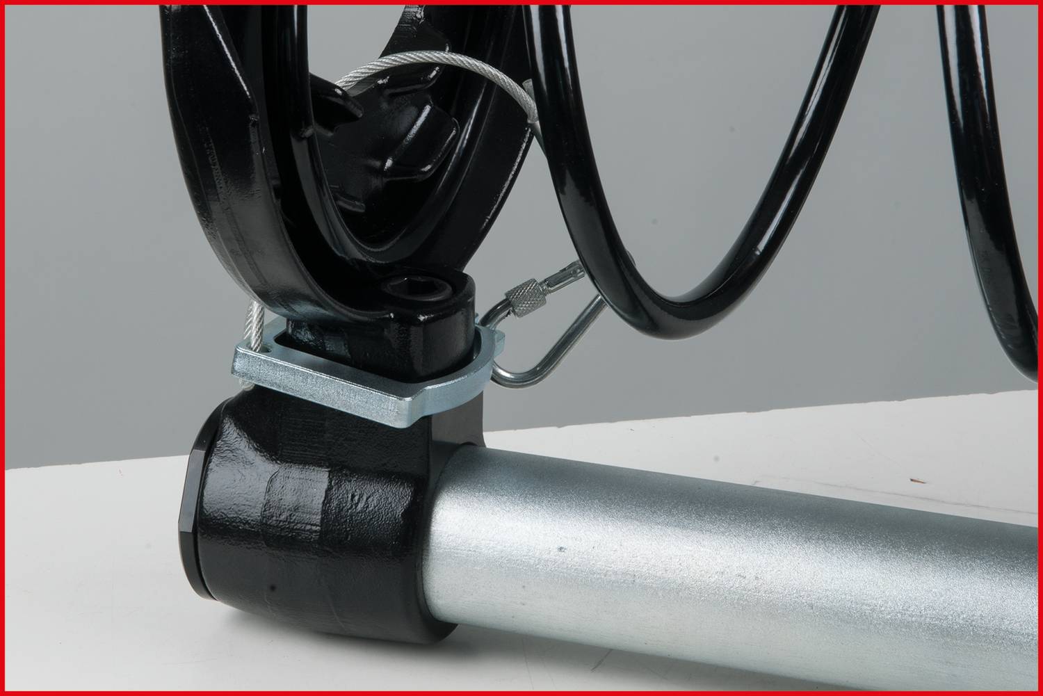 Nahaufnahme eines metallischen, spiralförmigen Fahrradschlosses, das um ein silbernes Rohr gewickelt ist. Das Schloss hat eine schwarze Ummantelung.