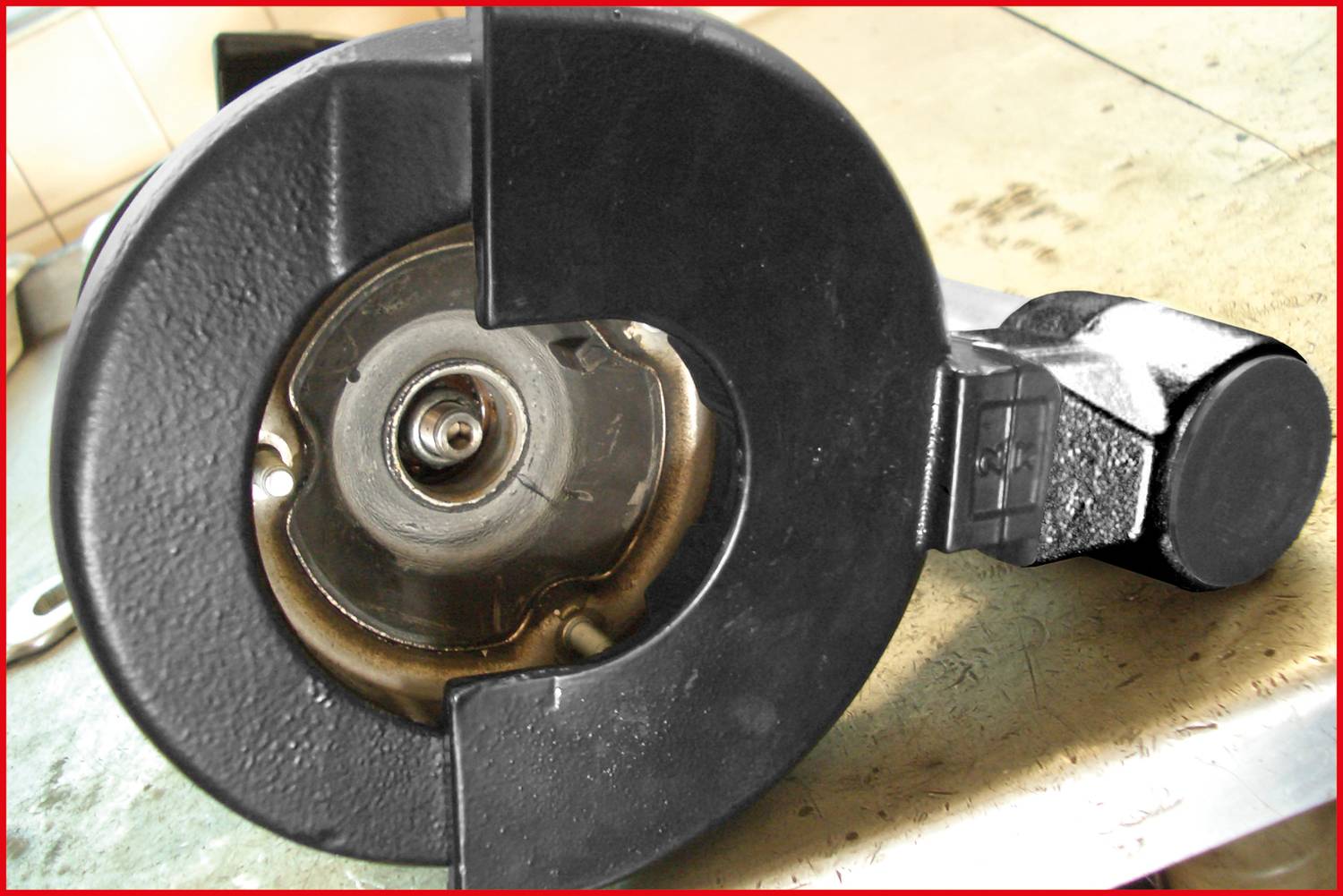 Nahaufnahme eines schwarzen Metallväderstoppers mit zylindrischem Mechanismus und robustem Gehäuse auf einem Werkstatttisch.