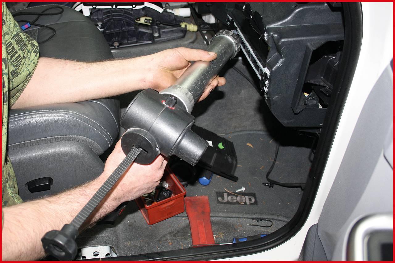 Ein Mechaniker hält eine Lenksäule in einem Auto. Innenraumdetails wie Sitze und Autozubehör sind sichtbar.