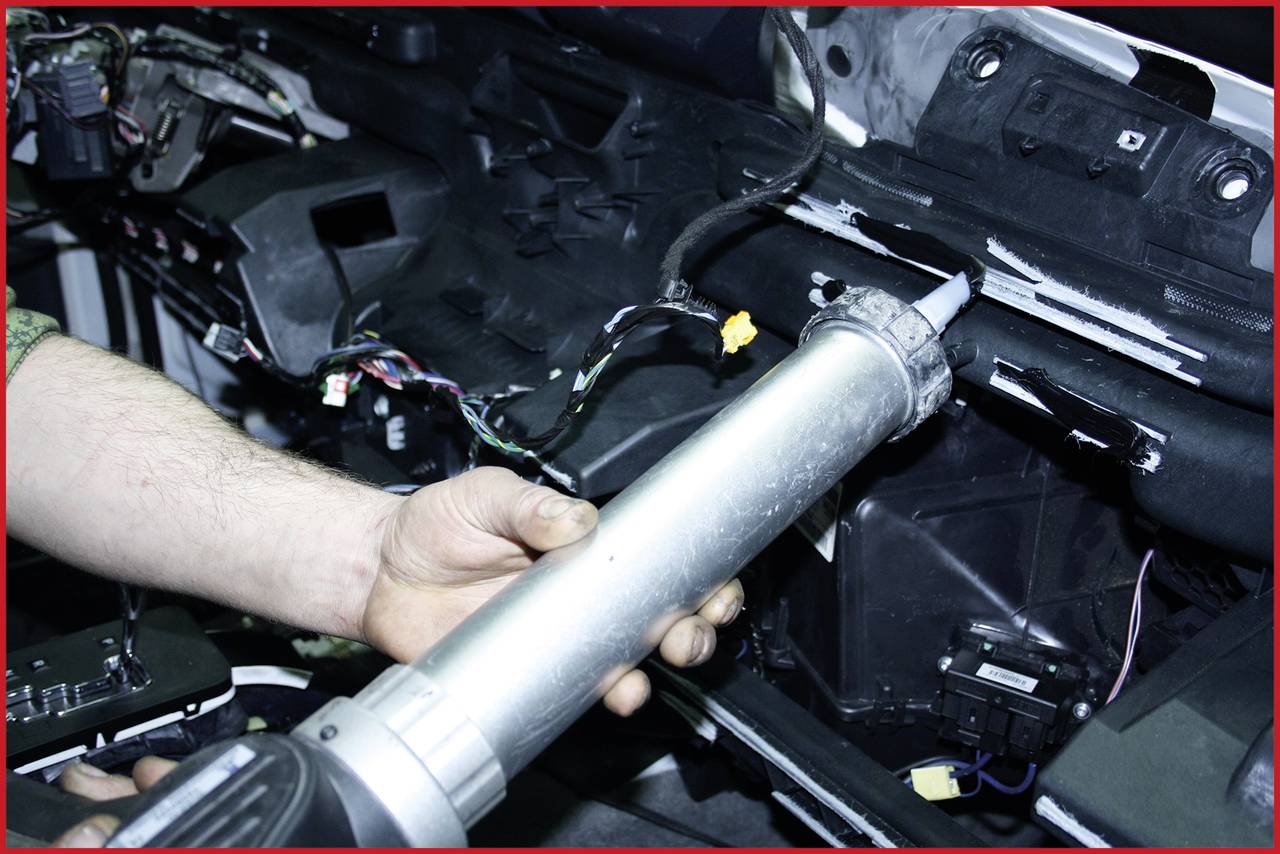 Eine Person hält eine Versiegelungspistole und trägt Dichtmittel auf einen Teil eines Autos im Innenraum auf, um Reparaturen durchzuführen.