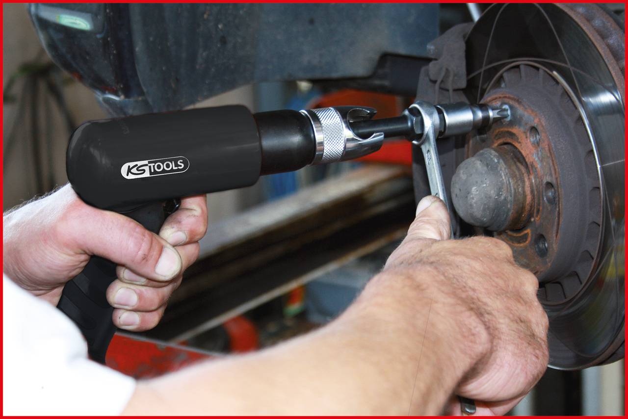 Eine Person verwendet ein Druckluftwerkzeug, um an einer Bremsscheibe zu arbeiten. Das Werkzeug trägt die Marke 'KS Tools'.