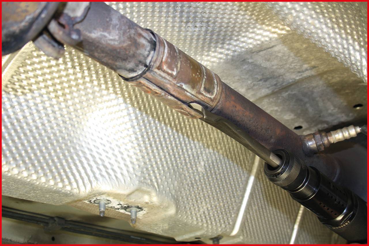 Rostiges Rohrfleck unter einem Fahrzeugboden, umgeben von hitzebeständigem Isoliermaterial; Zustand weist auf eventuelle Reparatur hin.