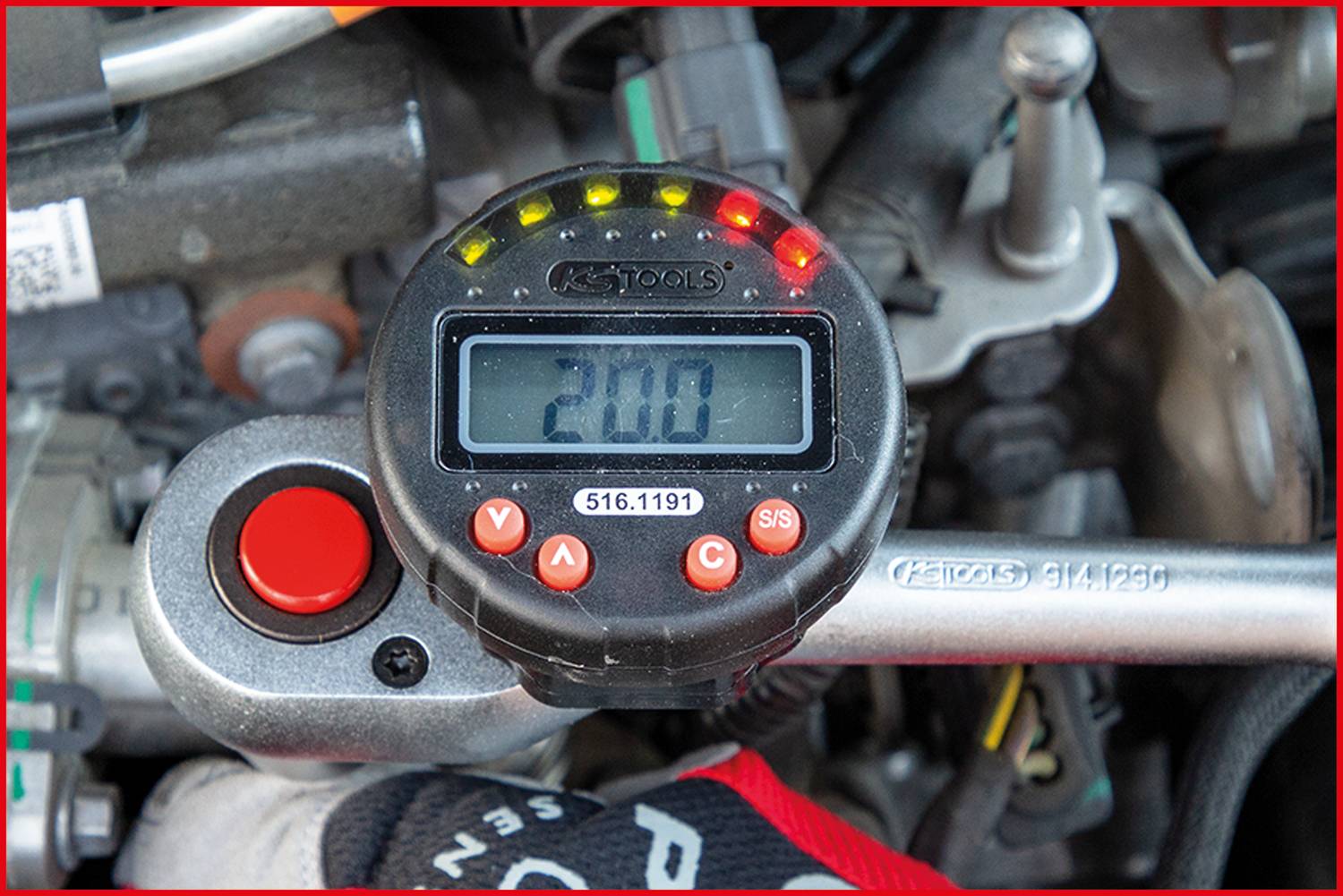 Ein Drehmomentschlüssel zeigt '20.0' auf einem digitalen Display an, umgeben von Motorteilen.