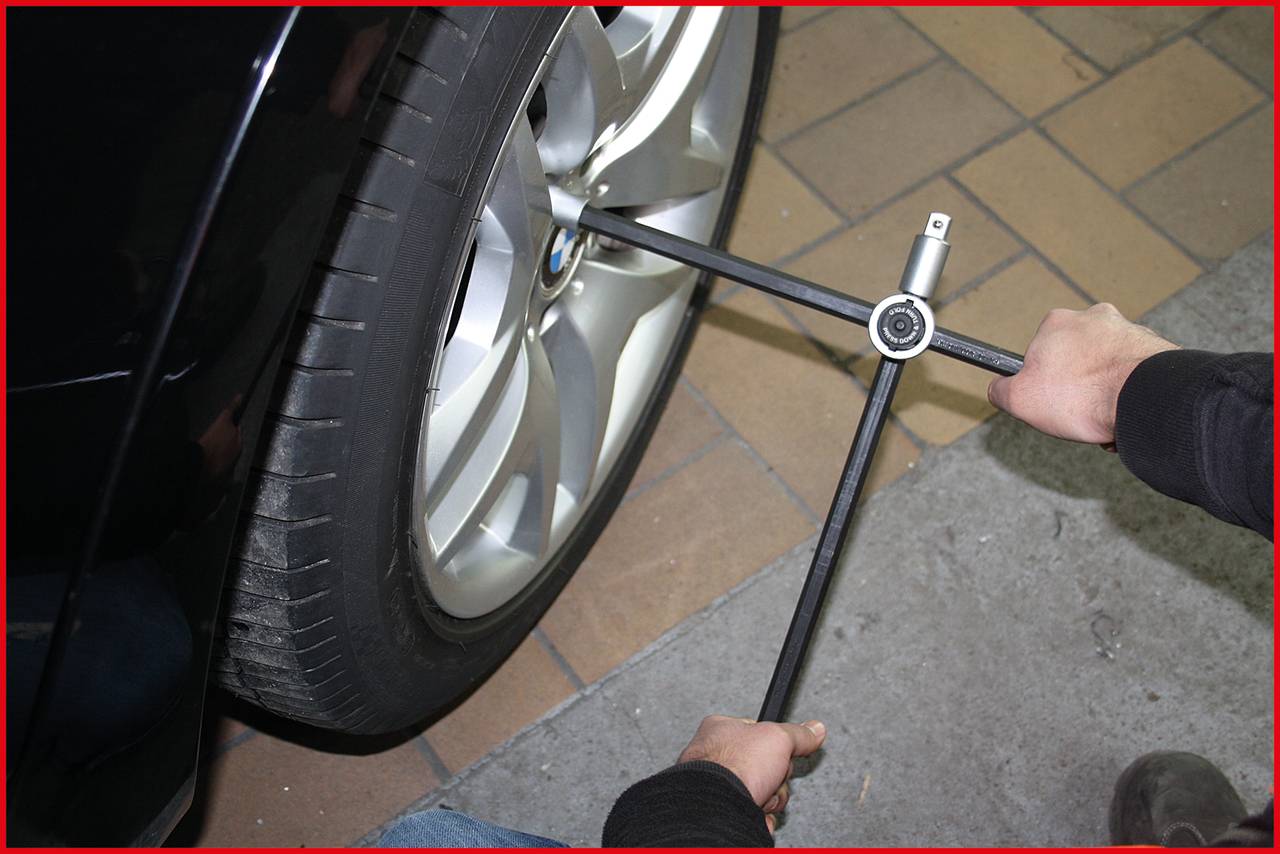 Person wechselt einen Autoreifen mit einem Kreuzschlüssel, indem sie die Radmuttern löst.