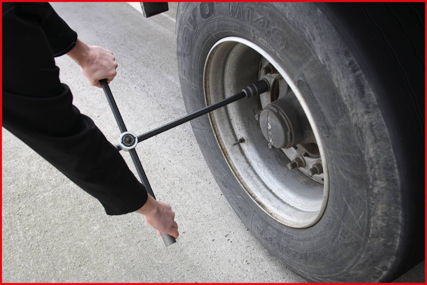 Eine Person wechselt einen Lkw-Reifen mit einem Kreuzschlüssel auf einer Betonfläche.