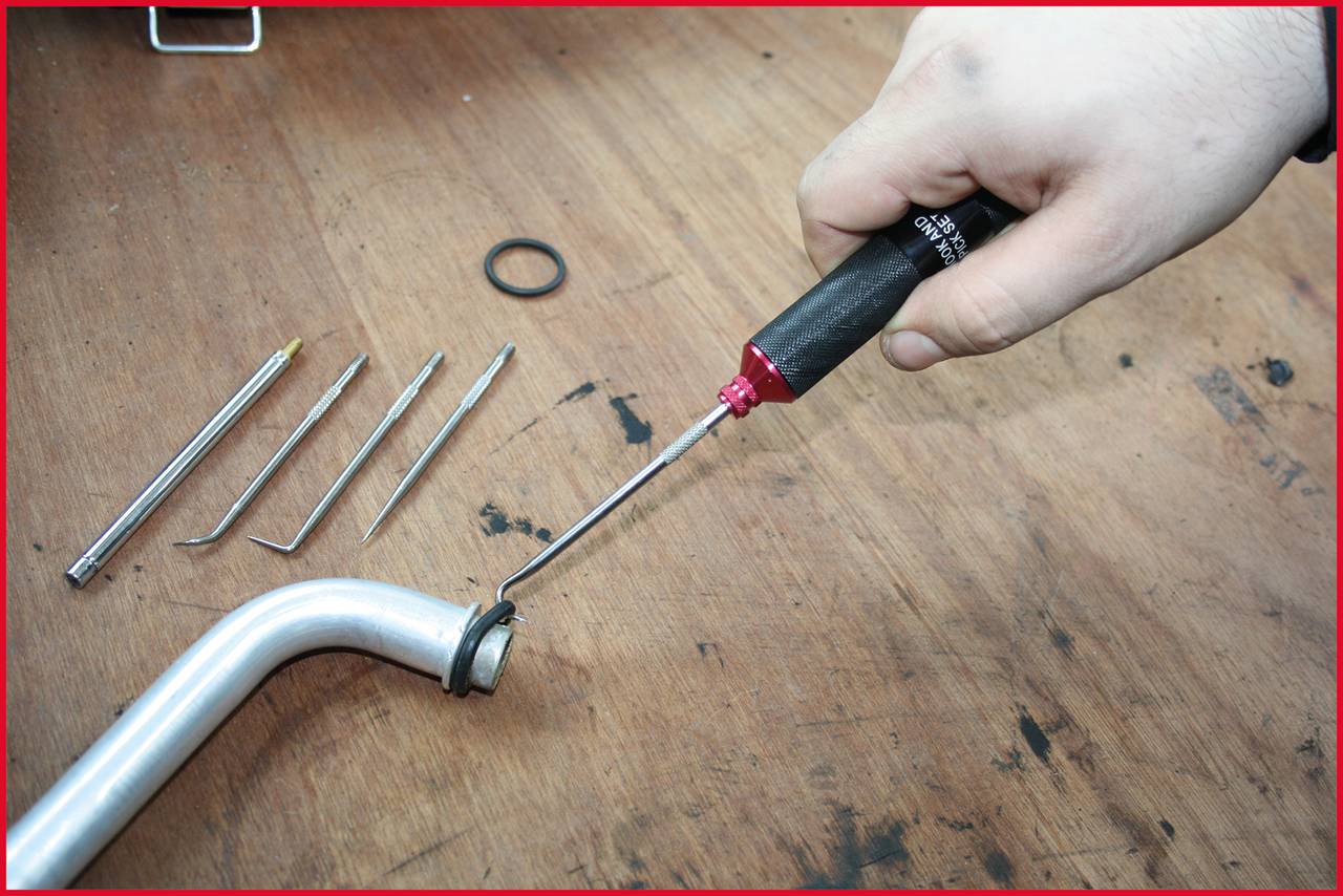 Eine Hand verwendet einen Schraubendreher, um ein kleines Metallteil an einem gebogenen Rohr auf einem Holztisch zu montieren.