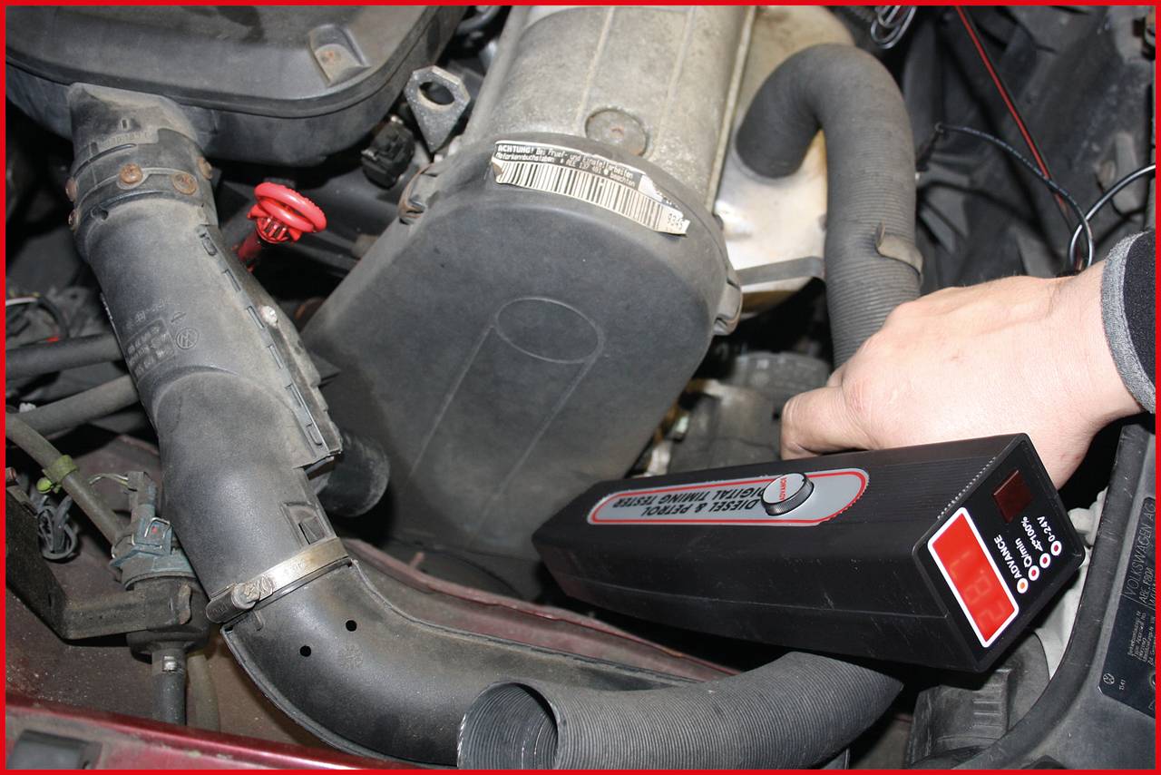 Eine Hand hält ein Diagnosetool zur Überprüfung des Motors in einem Auto. Der Motorraum ist gut sichtbar, das Tool zeigt eine Messung an.