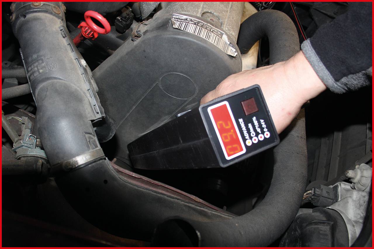 'Eine Person misst die Temperatur eines Autoteils mit einem digitalen Thermometer. Das Display zeigt 26°C an.'