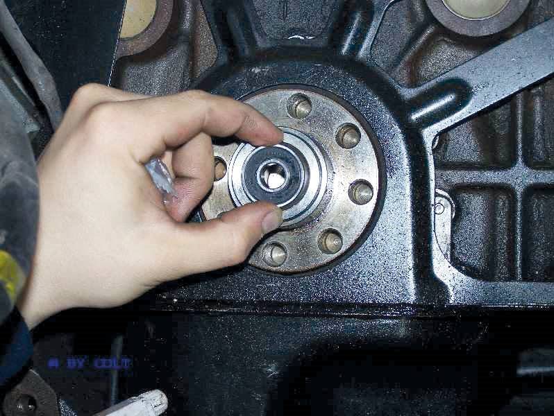 Eine Hand hält ein kleines, metallisches Zahnrad, das vor einem größeren Maschinenteil positioniert ist.