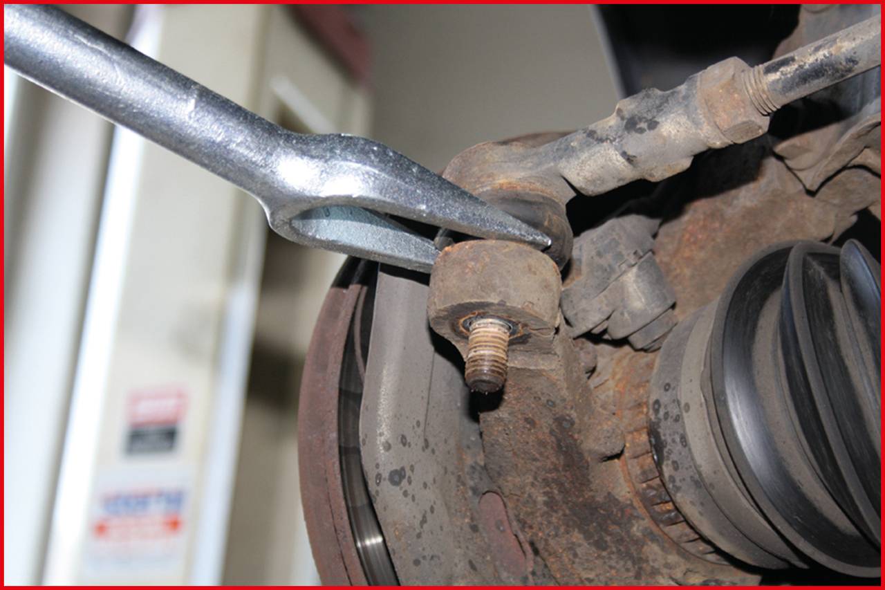 Ein Mechanikerwerkzeug hebelt eine verrostete Schraube an einem Fahrzeugteil auf, um Reparaturen an der Fahrzeugachse durchzuführen.